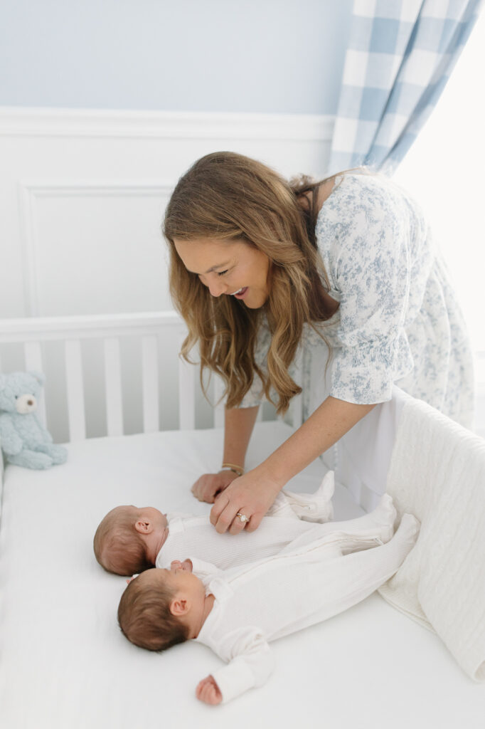 Mom smiling down towards her twins in a crib during Indianapolis newborn photos