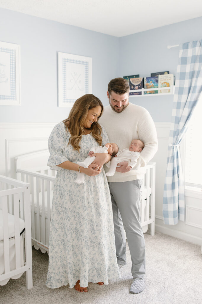 Parents holding twins and standing in nursery during indianapolis newborn photos