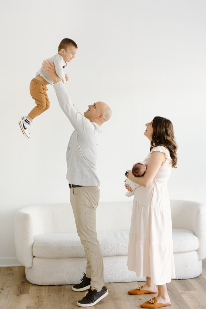 Dad lifting his son into the air and mom holding her newborn during indianapolis studio newborn photos
