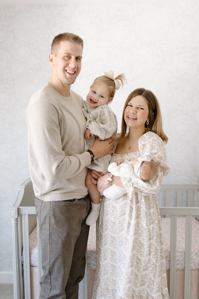 Parents holding toddler and newborn and smiling towards the camera during Indianapolis newborn photos