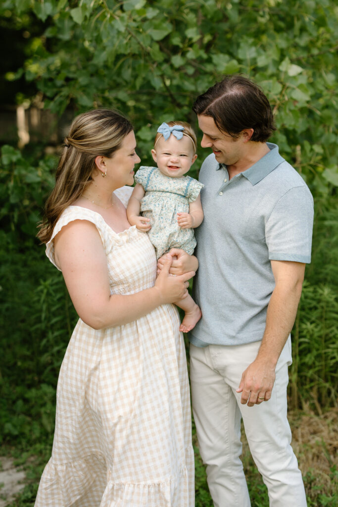 Little girl laughing towards camera while held by parents during Indianapolis Milestone Photography session