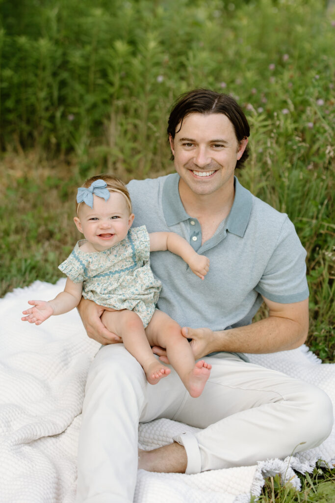 Dad and baby girl smiling towards camera and sitting on blanket during Indianapolis Milestone Photography session