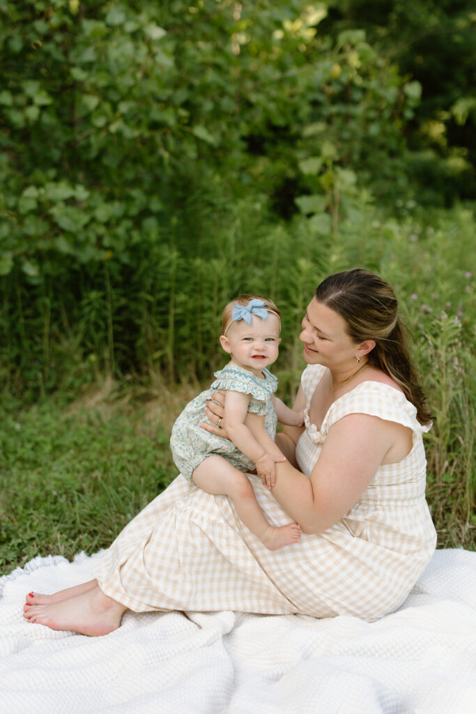Baby sitting on mom's knees and smiling towards the camera during Indianapolis Milestone Photography session