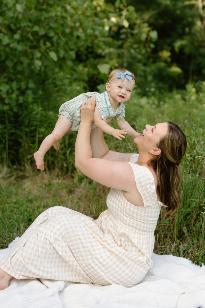 Mom lifting little girl while sitting on a blanket during Indianapolis Milestone Photography session