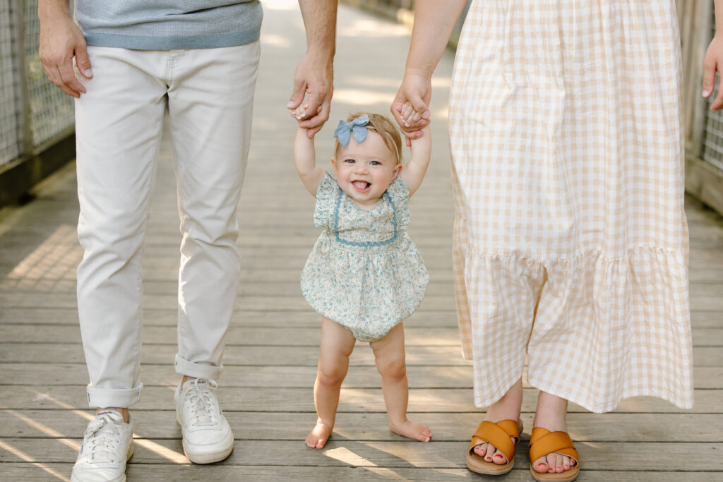 Baby smiling and holding onto parent's hands during Indianapolis Milestone Photography session