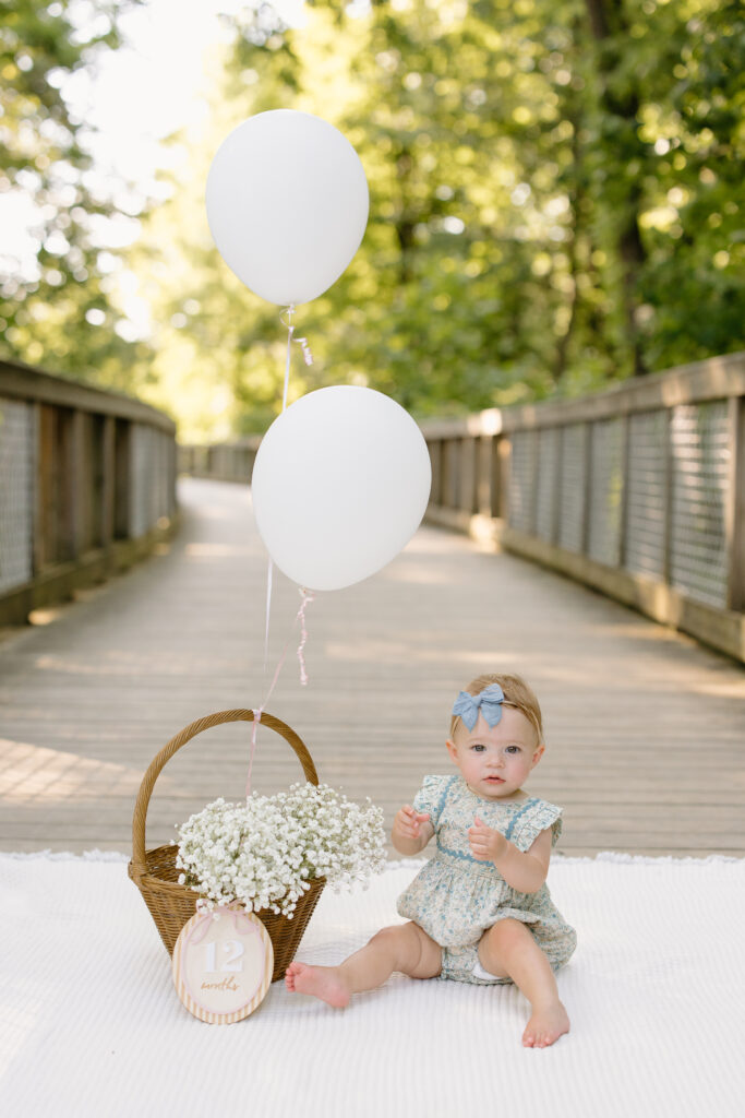 Baby looking towards camera while sitting on blanket with basket and balloons during Indianapolis Milestone Photography session