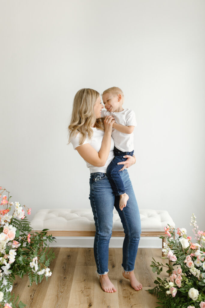 Mom holding hands with son and smiling towards him during Mother's Day Mini Sessions at Aspiring Eden Studio in Indianapolis