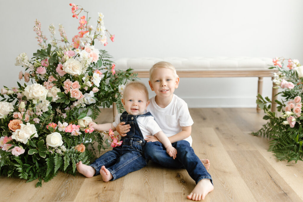 Boys smiling towards the camera and sitting on the ground during Mother's Day Mini Sessions at Aspiring Eden Studio in Indianapolis