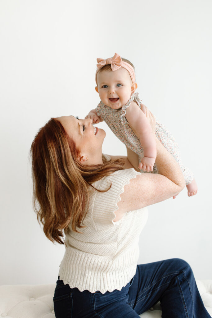 Baby girl smiling to camera while being lifted by mom during Mother's Day Mini Sessions at Aspiring Eden Studio in Indianapolis