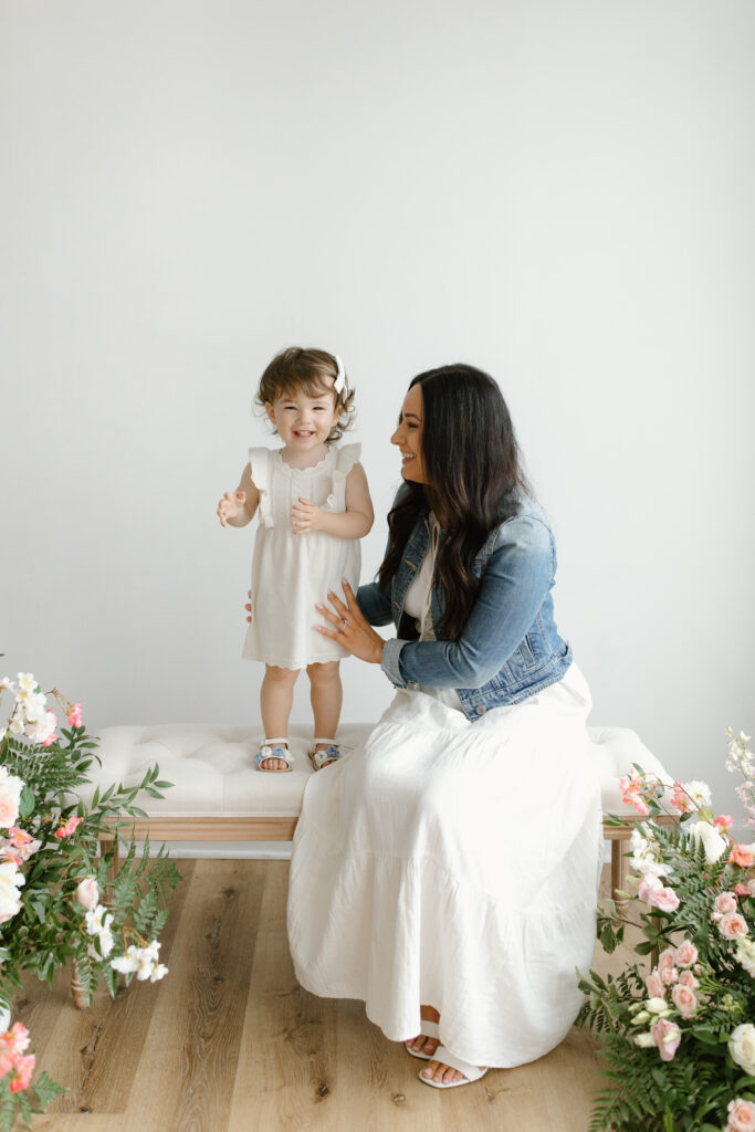 Little girl standing on bench and smiling to camera during Mother's Day Mini Sessions at Aspiring Eden Studio in Indianapolis