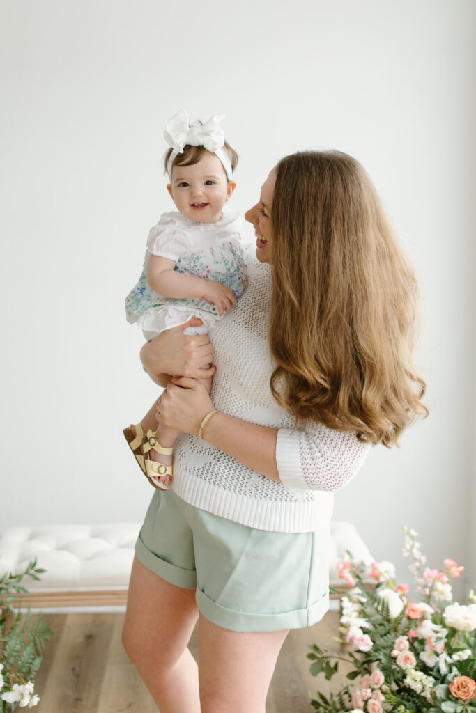 Little girl smiling to the camera while mom is holding her during Mother's Day Mini Sessions at Aspiring Eden Studio in Indianapolis