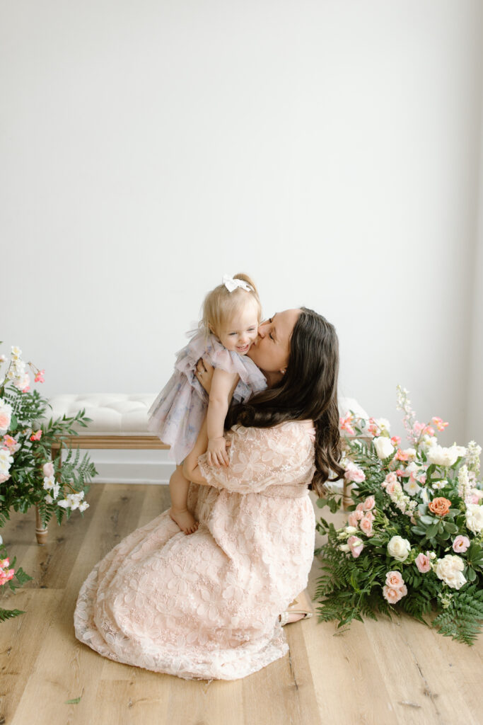 Mom kissing her daughter while sitting on the floor during Mother's Day Mini Sessions at Aspiring Eden Studio in Indianapolis