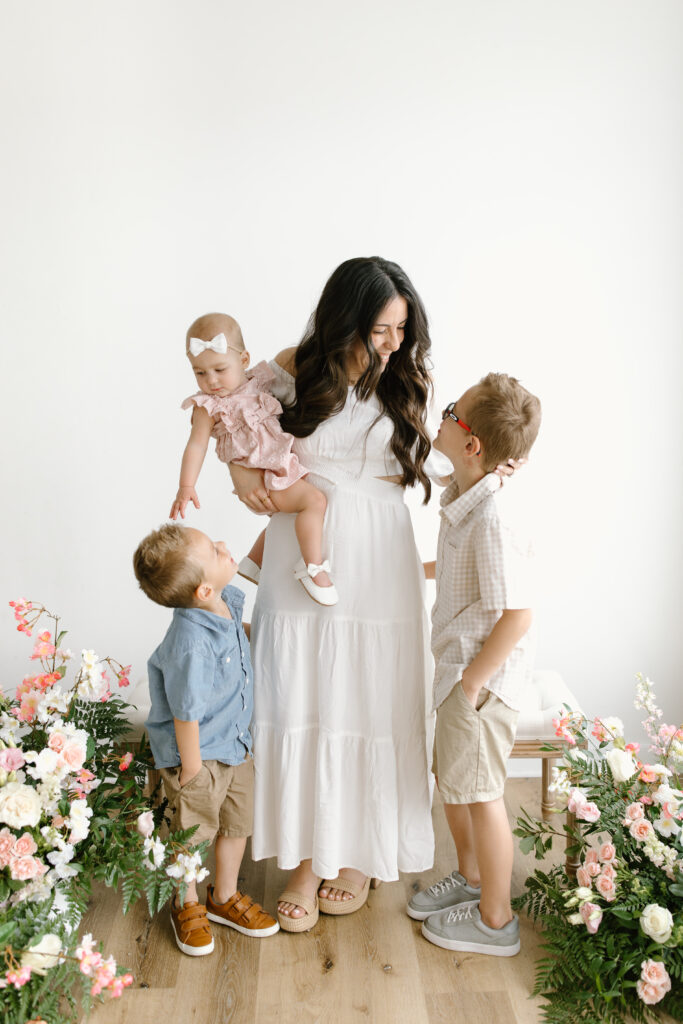 Mom holding her daughter and smiling towards her sons during Mother's Day Mini Sessions at Aspiring Eden Studio in Indianapolis
