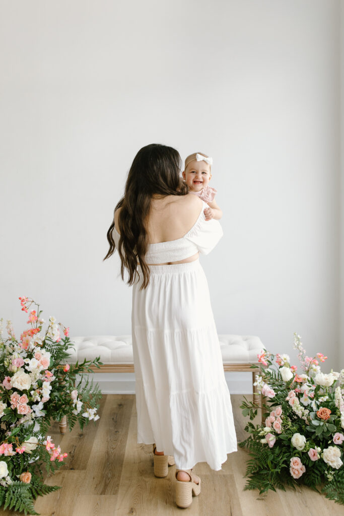 Mom walking away from camera while holding daughter during Mother's Day Mini Sessions at Aspiring Eden Studio in Indianapolis