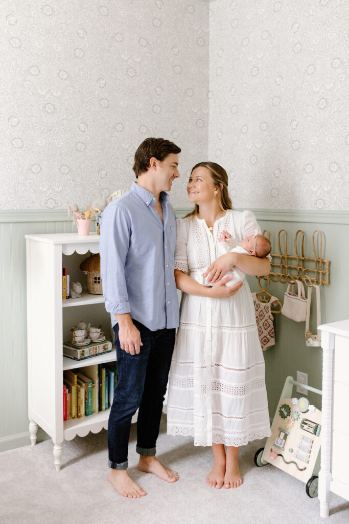 parents smiling towards each other and holding baby during newborn photos in Fishers, IN