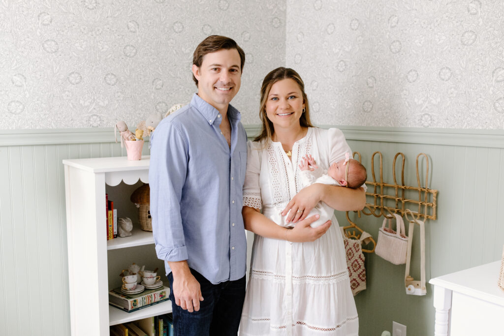parents holding newborn and smiling towards the camera during newborn photos in Fishers, IN