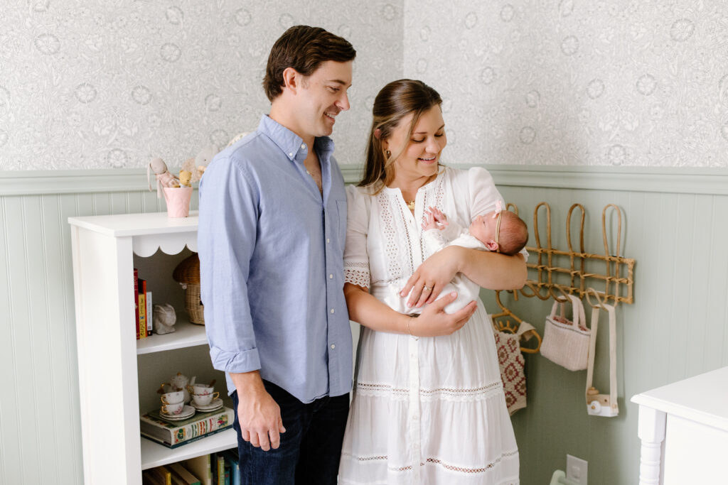 parents holding newborn and looking down towards her during newborn photos in Fishers, IN