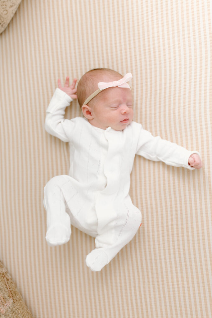 baby girl lying on stripped crib sheet during newborn photos in Fishers, IN