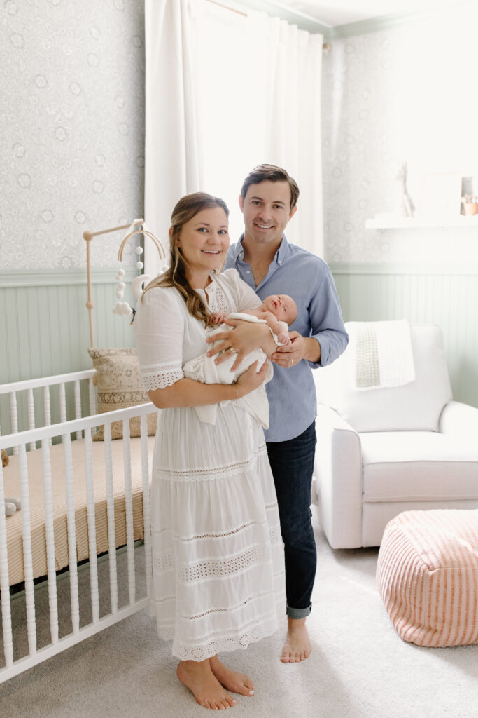 parents holding baby by crib during newborn photos in Fishers, IN