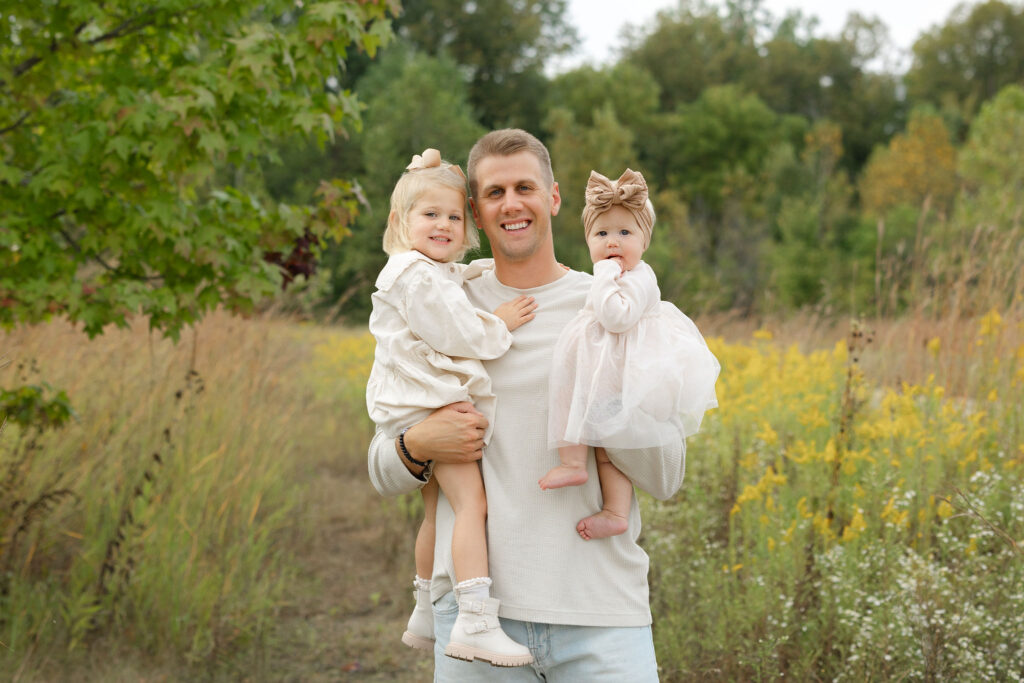 Dad holding daughters during fall family photos at West Park in with Capturing Simplicity Photography