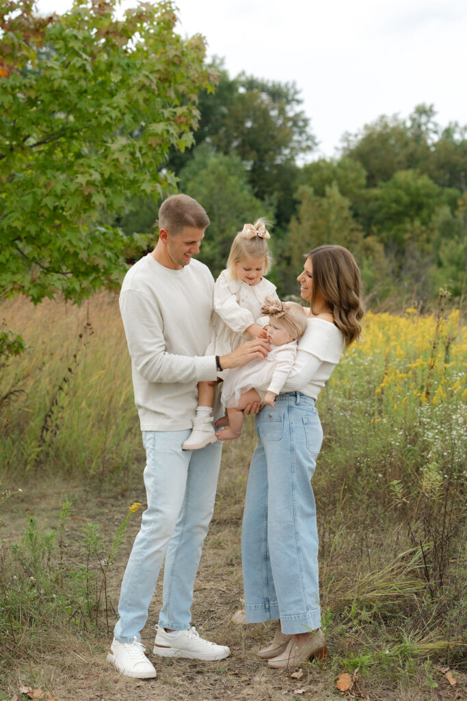 Sisters playing while held by parents during fall family photos at West Park in with Capturing Simplicity Photography