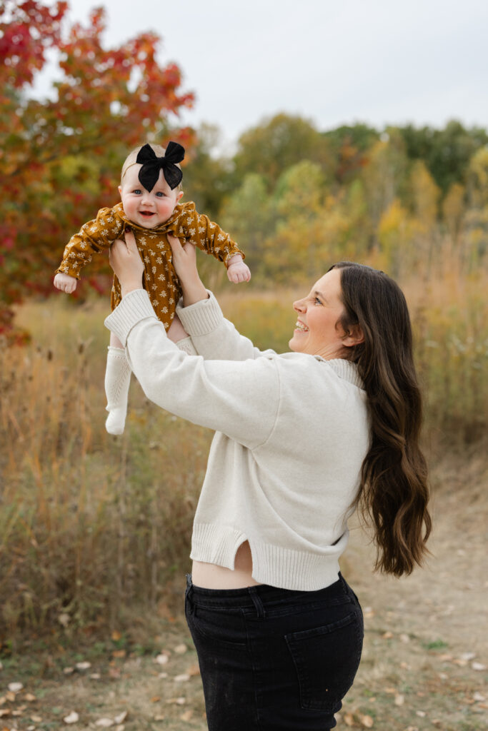 Baby girl lifted in air during Fall Mini Sessions at West Park with Capturing Simplicity Photography