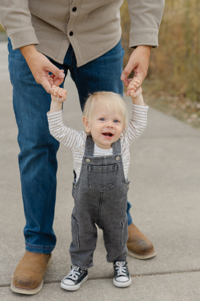 Baby boy walking with dad during Fall Mini Sessions at West Park with Capturing Simplicity Photography