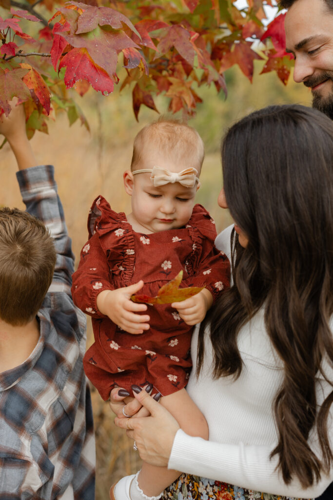 Little sister playing with leaves during Fall Mini Sessions at West Park with Capturing Simplicity Photography