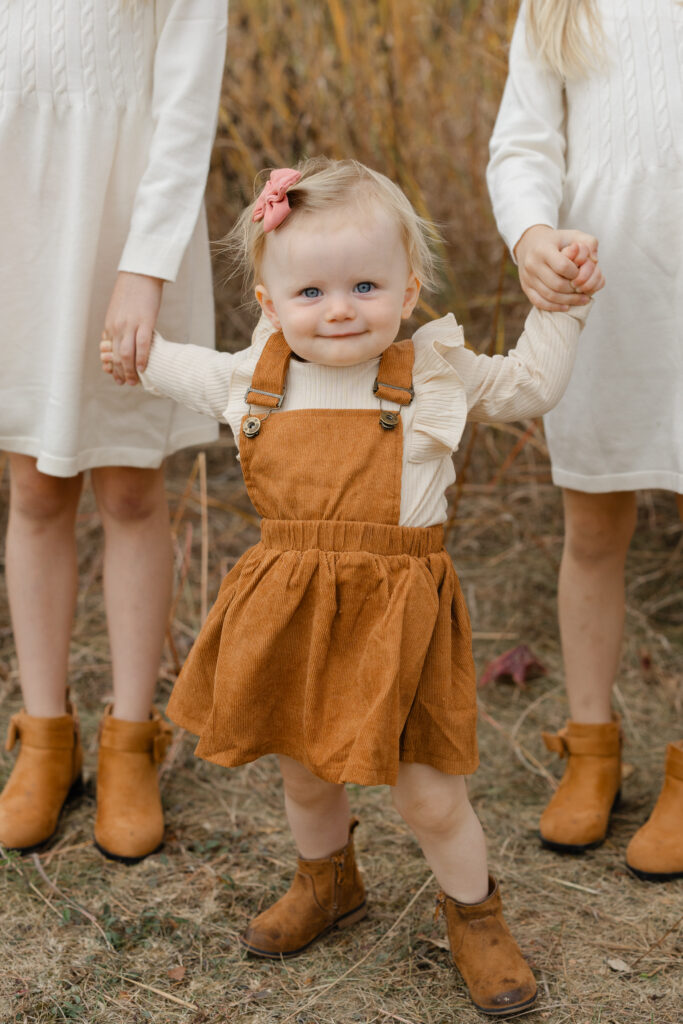 Little sister holding sisters hands during Fall Mini Sessions at West Park with Capturing Simplicity Photography