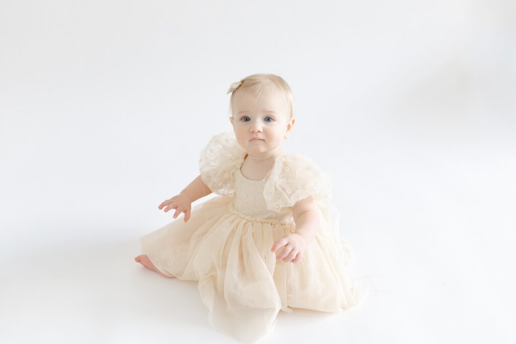 Baby girl sitting in tan dress during first birthday photos in downtown Indianapolis studio with Capturing Simplicity Photography
