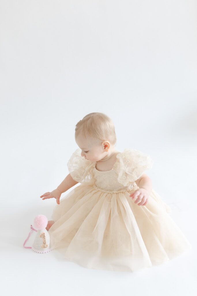 Little girl reaching for her 1st birthday hat during photos with Capturing Simplicity Photography
