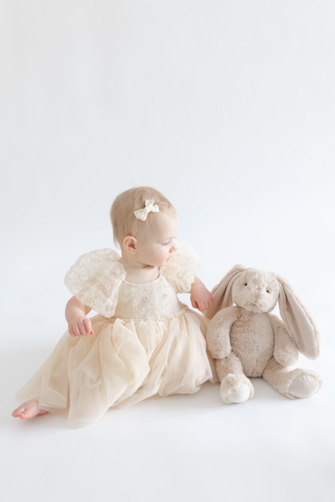 Baby girl sitting and looking towards her stuffed bunny during first birthday photos in Indianapolis with Capturing Simplicity Photography