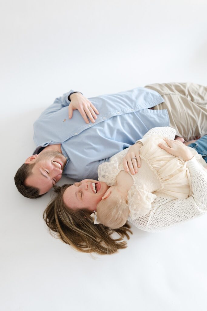 Parents lying down and snuggling with daughter during first birthday photos in Indianapolis studio with Capturing Simplicity Photography