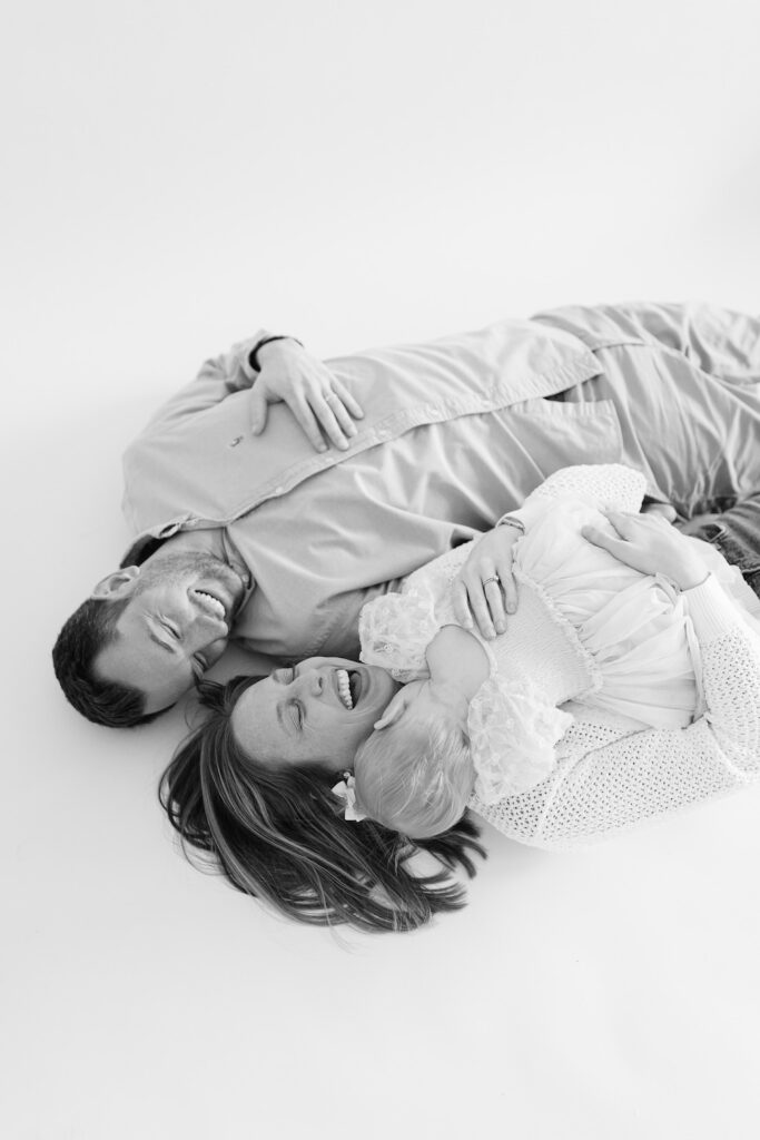 Black and white photo of mom and dad snuggling their daughter while lying on the ground during first birthday photos in Indianapolis with Capturing Simplicity Photography