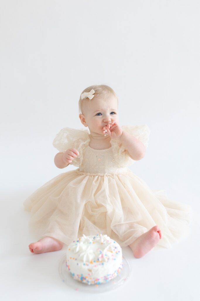 Little girl eating cake during first birthday photos in Indianapolis with Capturing Simplicity Photography